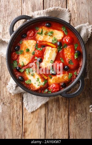 Mediterranean baked Halloumi with tomatoes, peppers, olives in a spicy sauce close-up in a pan on the table. Vertical top view from above