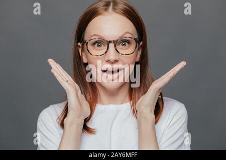 Wow, thats great! Surprised pleased beautiful woman has pleasant appearance, spreads palms near face, opens mouth from wonder, dressed in casual t shi Stock Photo