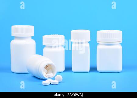 A line of white plastic medicine bottles and one in the foreground with pills spilling out. Stock Photo