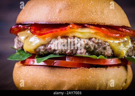 Craft beef burger with cheese, italian peperoni, tomato and basil leafs on wood table and rustic background Stock Photo