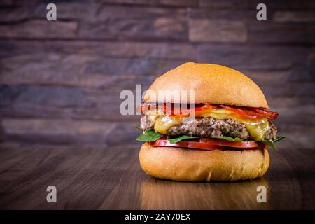 Craft beef burger with cheese, italian peperoni, tomato and basil leafs on wood table and rustic background Stock Photo