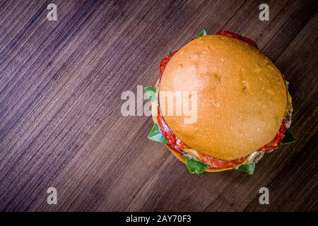 Craft beef burger with cheese, italian peperoni, tomato and basil leafs on wood table and rustic background Stock Photo