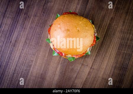 Craft beef burger with cheese, italian peperoni, tomato and basil leafs on wood table and rustic background Stock Photo