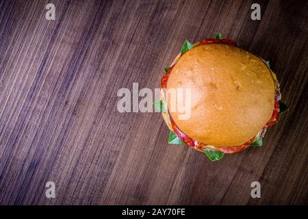 Craft beef burger with cheese, italian peperoni, tomato and basil leafs on wood table and rustic background Stock Photo