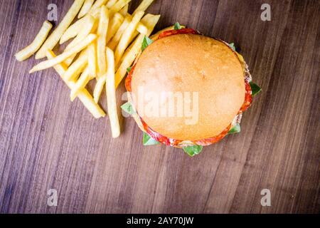Craft beef burger with cheese, italian peperoni, tomato, basil leafs and french fries on wood table and rustic background Stock Photo