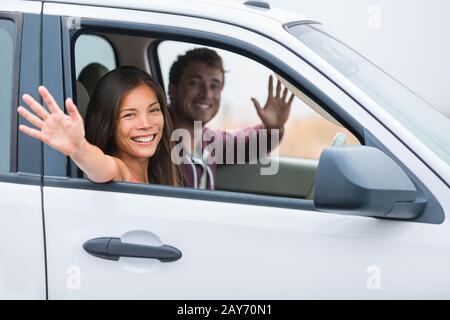 Happy multiracial couple on car travel together on summer vacation. Joyful young people smiling waving hello driving on road trip holidays. New young owners. Stock Photo
