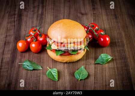 Craft beef burger with cheese, italian peperoni, tomato and basil leafs on wood table and rustic background Stock Photo