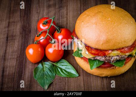 Craft beef burger with cheese, italian peperoni, tomato and basil leafs on wood table and rustic background Stock Photo