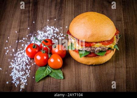 Craft beef burger with cheese, italian peperoni, tomato and basil leafs on wood table and rustic background Stock Photo