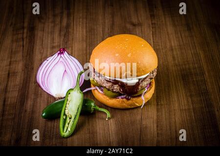 Craft beef burger with cream cheese, purple onion, jalapeno pepper on wood table and rustic background Stock Photo