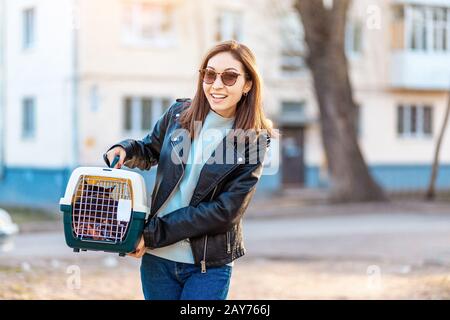 Girl pet owner carries her cat in a special plastic cage carrier for a walk or in a veterinary clinic Stock Photo