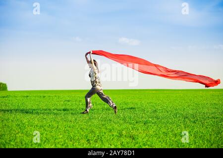 Beautiful young woman jumping on a green meadow with colored tissue Stock Photo