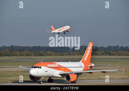 Two EasyJet planes at London Stansted Airport - one taxing to the runway as another one departs in the background