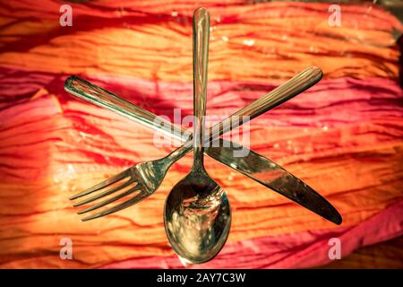 Fork, spoon and knife crossed against colorful background Stock Photo