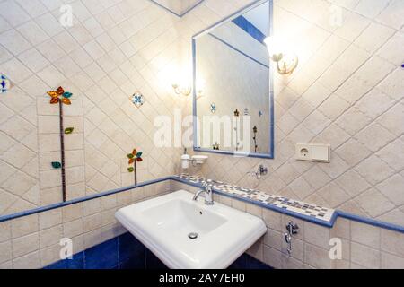 Sink and mirror in an expensive bathroom with white square tiles with uneven edges and a floral pattern. Stock Photo