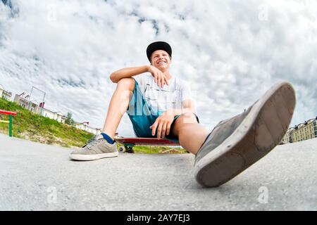 Young skater resting sitting on his skateboard in a skatepark Stock Photo