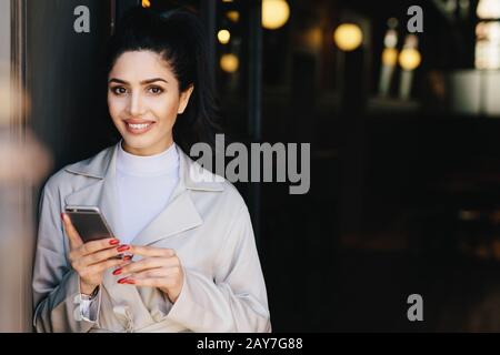Attractive brunette businesswoman having dark hair tied in pony tail and wonderful make-up smiling demonstrating her white perfect teeth waitng for he Stock Photo