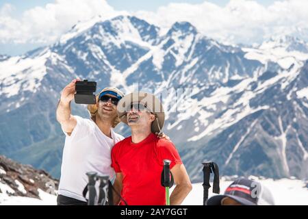 Two hickers taking selfie in the snow-capped mountains against the background of rocks and glaciers Stock Photo