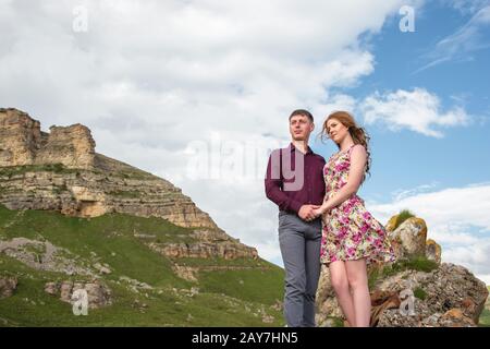 couple Young guy with a girl holding hands standing and looking away in the background of a beautiful landscape of rocks and clo Stock Photo