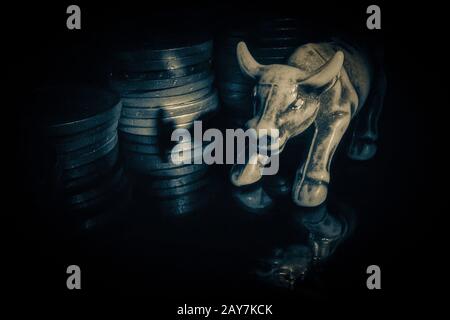 Bull figurine on a black reflective surface on a background of coins.The symbol of the upward trend.Market.Forex. Stock Photo