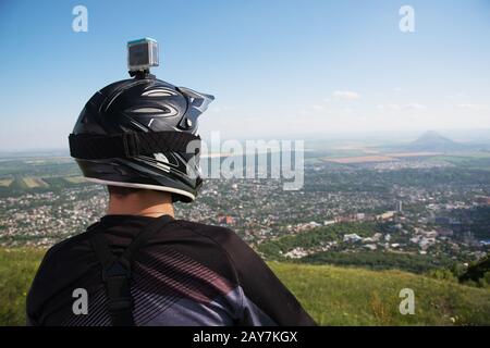 View from the back. MTB rider looks from the mountain to the city which is somewhere down there Stock Photo
