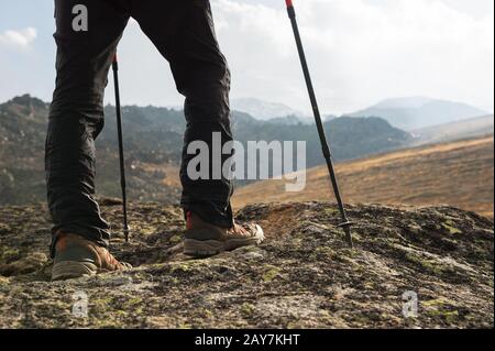 Close-up of male legs in trekking boots with sticks for Nordic walking against the background of rocks and distant Caucasian lan Stock Photo