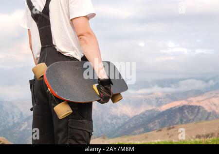 A young man in a helmet wearing gloves with a board in his hands and dressed in a combo stands on a precipice high in the mounta Stock Photo