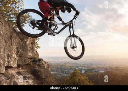 a young rider at the wheel of his mountain bike makes a trick in jumping on the springboard of the downhill mountain path in the Stock Photo