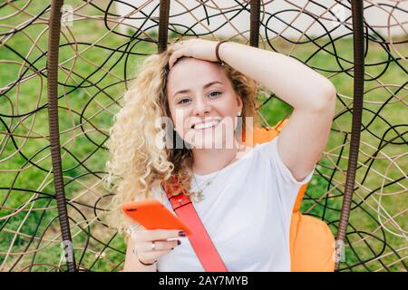 Smiling European female with broad smile, curly hair, dressed in casual white t shirt, uses modern electronic device for surfing social networks, happ Stock Photo