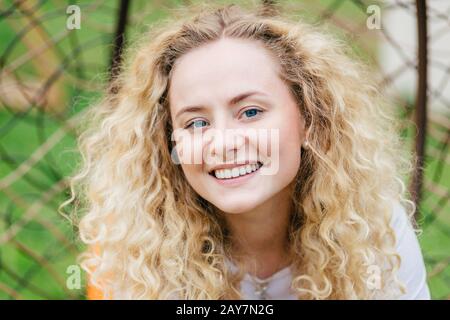 Close up portrait of romantic beautiful fair haired female with appealing smile, rests outdoor, being in good mood, feels inspired by beauty of nature Stock Photo