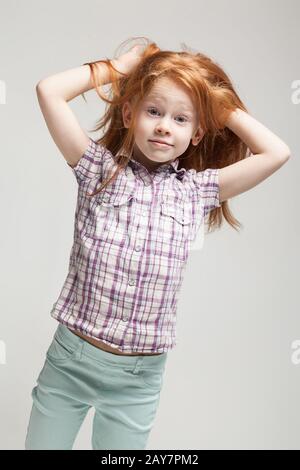 Beautiful redhead little girl in plaid shirt, bright blue trousers and white boots