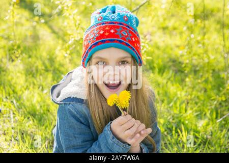 Seven-year-old girl in the spring is pleased with the blossoming dandelions Stock Photo