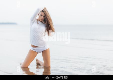 Slim appealing gorgeous woman wears white summer clothing, poses against beautiful sea view, keeps hand on head, breathes fresh air, copy space for yo Stock Photo