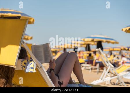 Summer holidaymaker reading a book on a sun lounger on a sandy beach Stock Photo