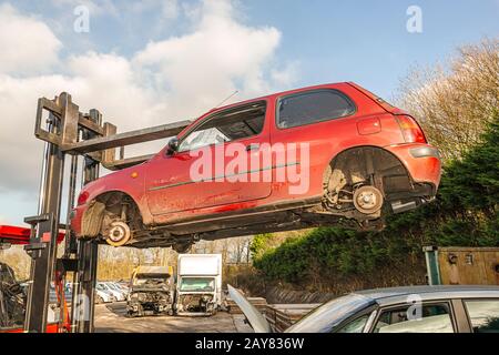 car wreck hanging from a lift truck high in the air on a dismantling site Stock Photo