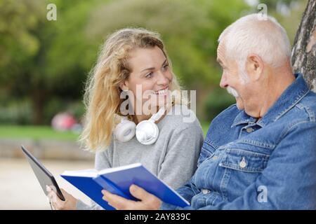 smiling nurse reading book to senior man outdoor Stock Photo