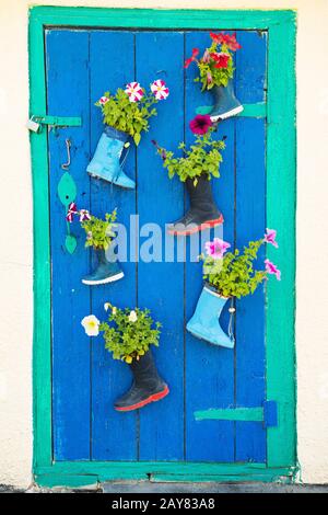 Old children rubber boots with blooming summer flowers on the entrance door of a house Stock Photo