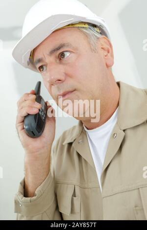 male builder in a helmet using a walkie talkie Stock Photo