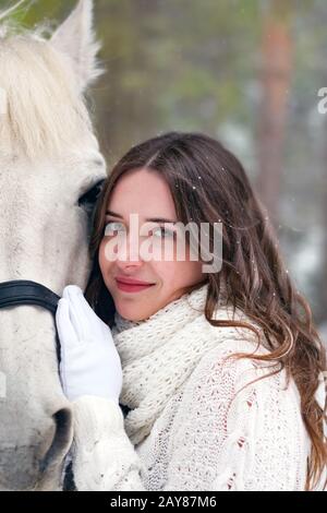 Portrait of a young, beautiful girl in close-up with a white horse in winter Stock Photo