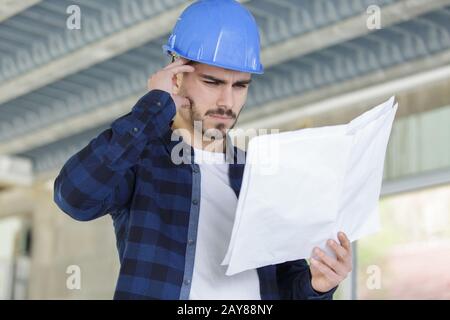 thoughtful young worker with plans indoors Stock Photo