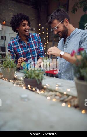 two guys, adult young men, talking and laughing in a bar with drinks in their hands. friendship, socializing, leisure, meeting, multiethnic Stock Photo