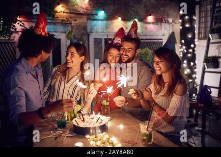 friends at birthday party with handheld fireworks in their hands, talking, laughing. friends, social, togetherness, birthday party concept Stock Photo