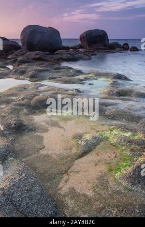 stone on seashore at sunset with a wave Stock Photo