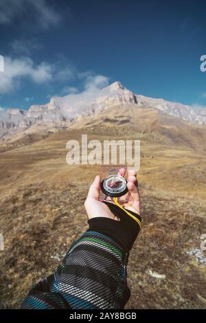 Viewpoint shot. A first-person view of a man's hand holds a compass against the background of an epic landscape with cliffs hill Stock Photo