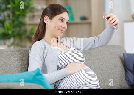 Delighted pregnant woman making selfie in bed room Stock Photo - Alamy