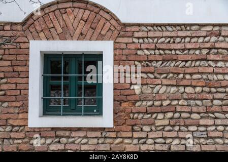 Window with window grille in the middle of a brick wall of bricks and river stones Stock Photo