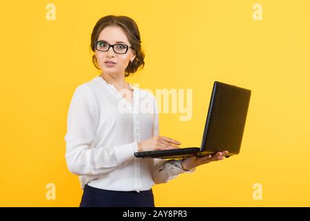 Portrait of confident beautiful young confused business woman working on laptop on yellow background Stock Photo