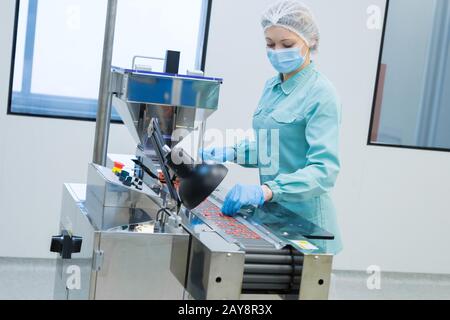 Pharmacy industry woman worker in protective clothing operating production of tablets in sterile working conditions Stock Photo