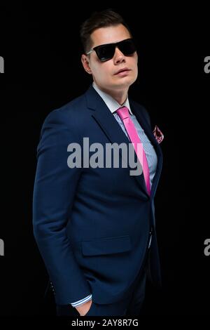 Portrait of confident handsome businessman in sunglasses on black background with hands in pockets Stock Photo
