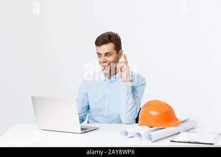 Handsome male engineer is using a notebook for work. He is sitting at the desk and smiling. Copy space on side. Stock Photo